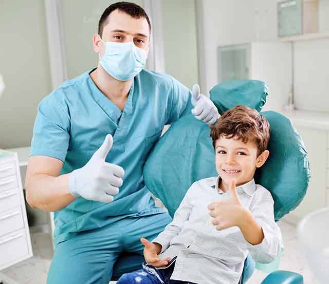 A dentist and a smiling young boy giving a thumbs up