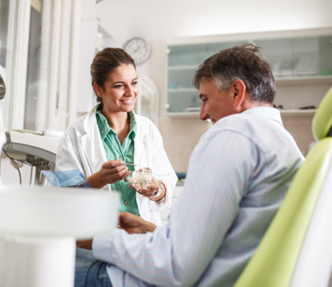 Smiling dentist showing patient model of teeth