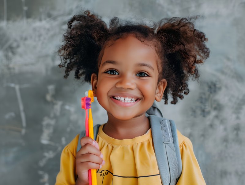 little girl with backpack and holding toothbrushes